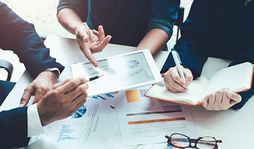 Pessoas discutindo e avaliando gr�ficos apontando para um tablet.